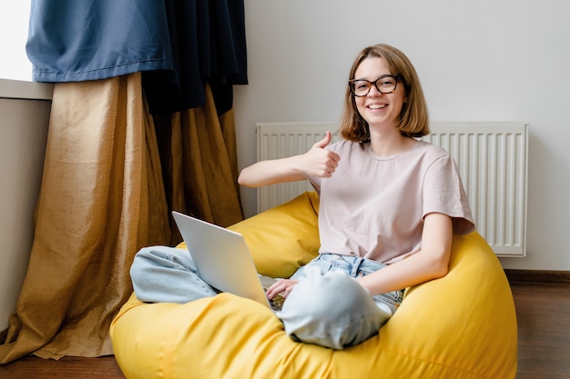 Jonge freelancervrouw die duim met laptop toont die online werkt