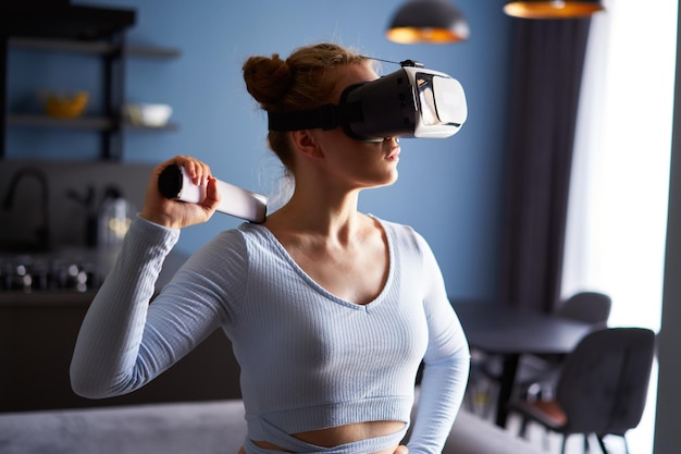 Jonge, futuristische blonde meid met een virtual reality-headset met een controller die een videogame speelt