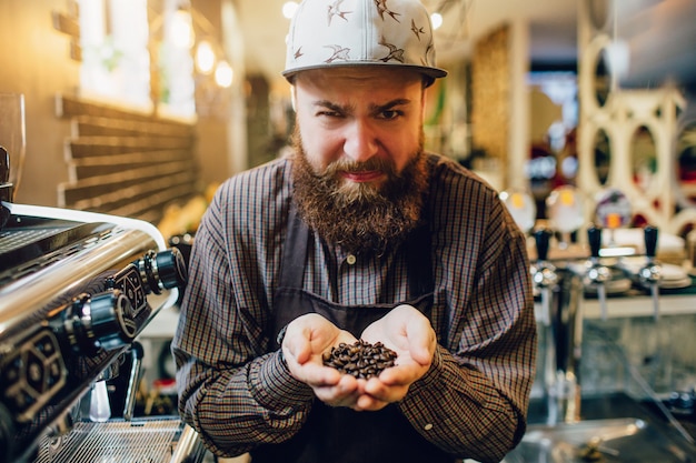 Jonge gebaarde barista houdt koffiebonen in handen en kijkt op camera