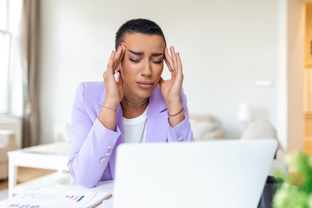 Jonge gefrustreerde vrouw die aan het kantoor werkt voor een laptop en dagelijks aan chronische hoofdpijn lijdt. Online behandeling. Afspraak voor een medisch consult. Elektromagnetische straling. Ziektevergoeding.