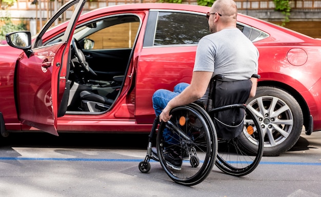 Jonge gehandicapte bestuurder die in rode auto van rolstoel krijgt.