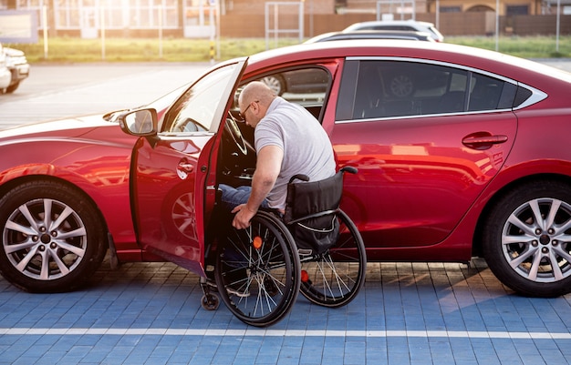 Jonge gehandicapte bestuurder stapt in rode auto uit rolstoel