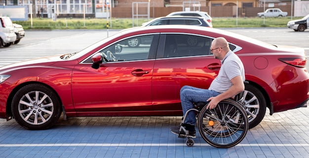 Jonge gehandicapte bestuurder stapt in rode auto uit rolstoel