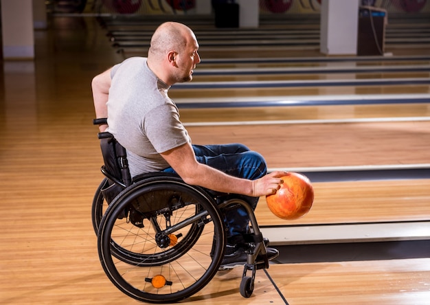 Jonge gehandicapte man in rolstoel bowlen in de club