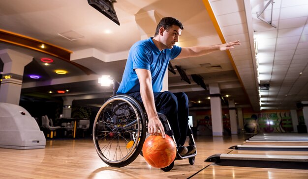 Jonge gehandicapte man in rolstoel bowlen in de club