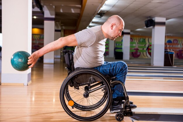 Jonge gehandicapte man in rolstoel bowlen in de club