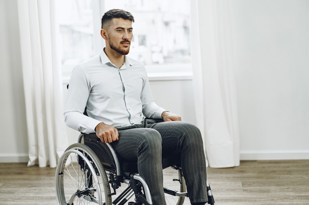 Jonge gehandicapte man zit in een rolstoel bij het raam thuis