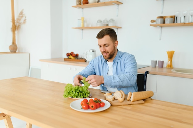 Jonge gehandicapte man zittend op een rolstoel eten bereiden in de keuken