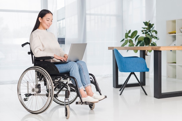 Jonge gehandicapte vrouwenzitting in een rolstoel die laptop met behulp van op het werk