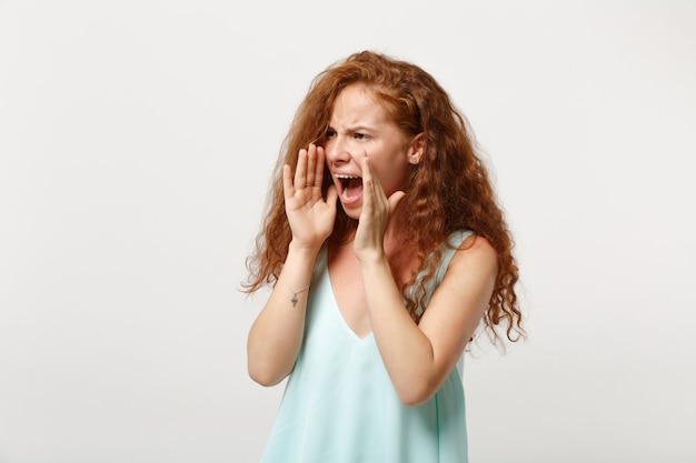 Jonge geïrriteerde roodharige vrouw in casual lichte kleding poseren geïsoleerd op een witte achtergrond in de studio. mensen levensstijl concept. bespotten kopie ruimte. opzij kijkend schreeuwend met handgebaar in de buurt van mond.