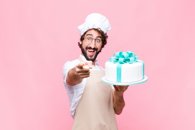 Jonge gekke bakkersmens die een cake houdt tegen roze muur