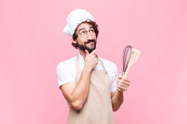 Jonge gekke bakkersmens met een kokhulpmiddel tegen roze muur