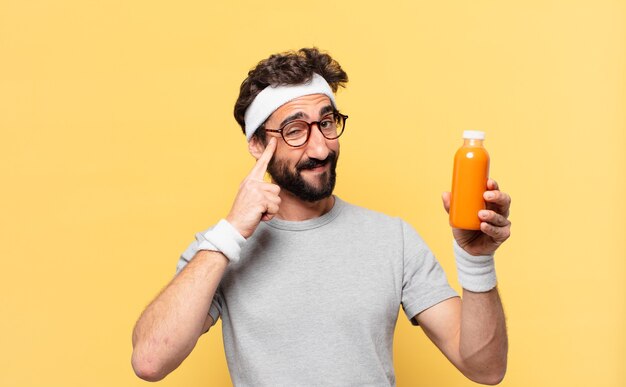 Jonge gekke bebaarde atleet die uitdrukking denkt en een smoothy vasthoudt