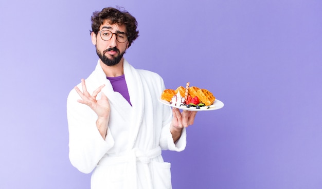 Jonge gekke bebaarde man badjas dragen en wafels hebben