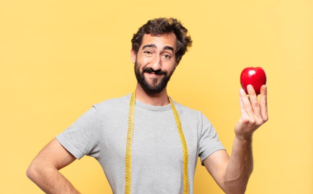 Jonge gekke bebaarde man die een gelukkige uitdrukking op dieet heeft en een appel vasthoudt