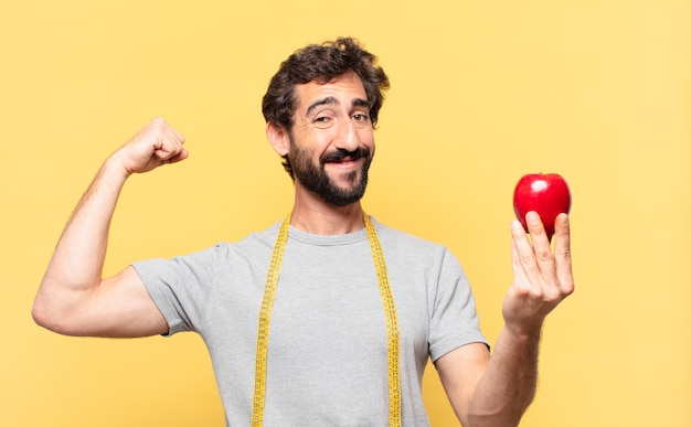 Jonge gekke bebaarde man die een gelukkige uitdrukking op dieet is en een appel vasthoudt