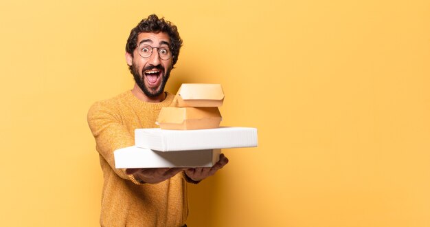 Jonge gekke bebaarde man die fastfood met een kopie ruimte heeft weggehaald