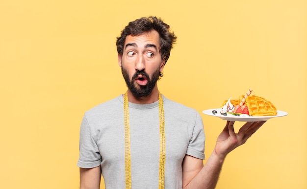 jonge gekke bebaarde man die op dieet is met een bange uitdrukking en wafels vasthoudt