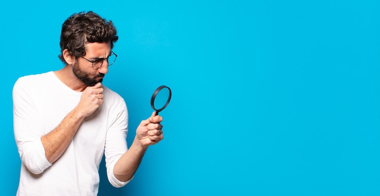 Foto jonge gekke bebaarde man die op zoek is en probeert te vinden met een vergrootglas