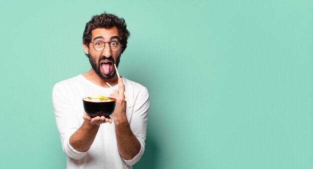 Jonge gekke bebaarde man met een noedel ramen kom