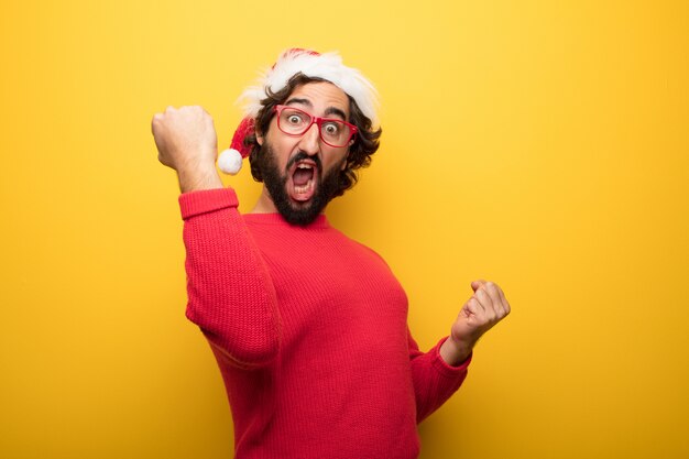 Jonge gekke bebaarde man met rode bril en hoed van de Kerstman