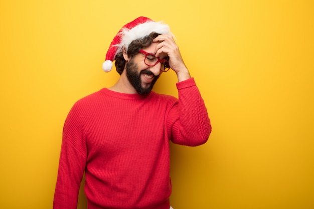 Jonge gekke bebaarde man met rode bril en hoed van de Kerstman