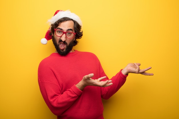 Jonge gekke bebaarde man met rode bril en hoed van de Kerstman