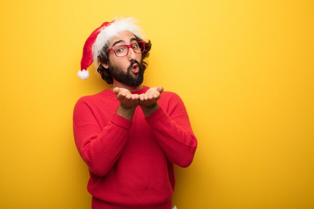 Jonge gekke bebaarde man met rode bril en hoed van de Kerstman