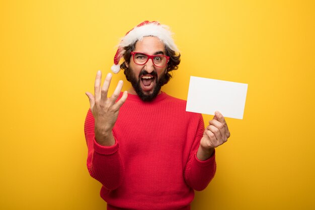 Jonge gekke bebaarde man met rode bril en hoed van de Kerstman