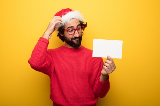 Jonge gekke bebaarde man met rode bril en hoed van de Kerstman