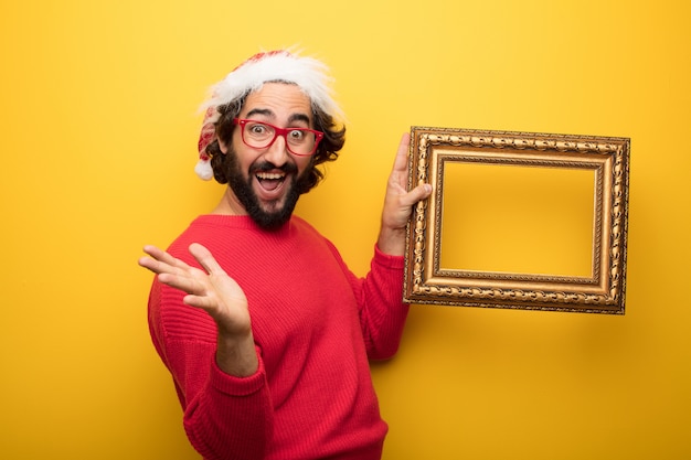 Jonge gekke bebaarde man met rode bril en hoed van de Kerstman