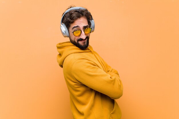 Jonge gekke koele mens het luisteren muziek met hoofdtelefoons tegen oranje muur