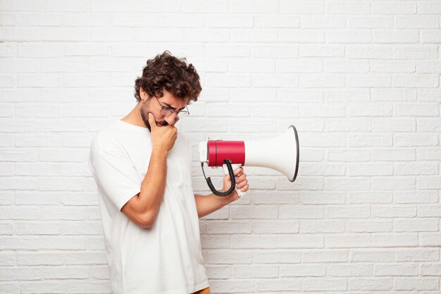 Jonge gekke man met een megafoon tegen de muur.