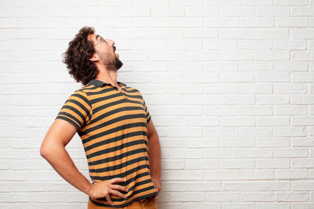 Jonge gekke of dwaze mens die en emoties tegen bakstenen muurachtergrond gesturing uitdrukken