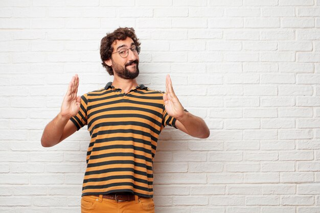 Jonge gekke of dwaze mens die en emoties tegen bakstenen muurachtergrond gesturing uitdrukken