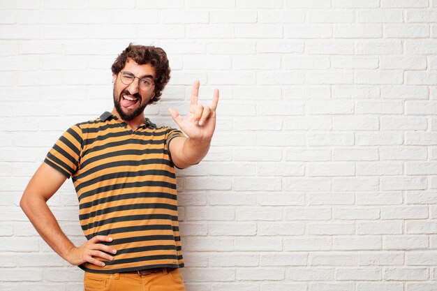 Jonge gekke of dwaze mens die en emoties tegen bakstenen muurachtergrond gesturing uitdrukken