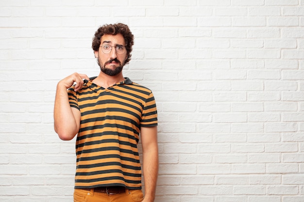 Jonge gekke of dwaze mens die en emoties tegen bakstenen muurachtergrond gesturing uitdrukken