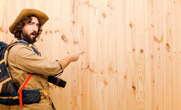 Jonge gekke ontdekkingsreiziger met strohoed en rugzak op houten muur