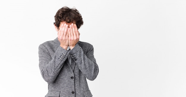 Jonge gekke zakenman die droevig, gefrustreerd, zenuwachtig en depressief voelen, die gezicht behandelen met beide handen, die tegen muur schreeuwen