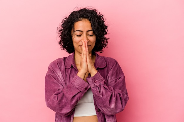 Jonge gekrulde latijnse vrouw geïsoleerd op roze achtergrond hand in hand in bidden in de buurt van mond, voelt zich zelfverzekerd.