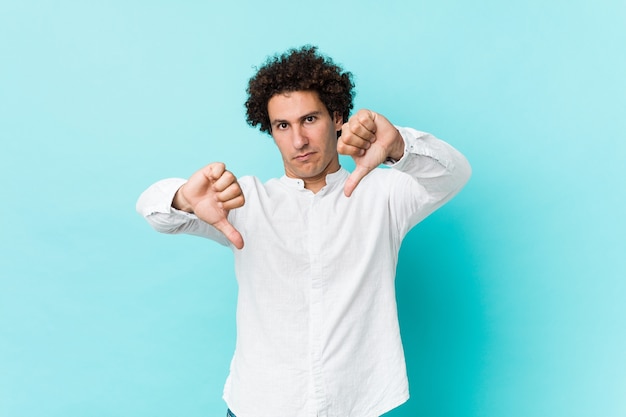 Jonge gekrulde volwassen man met een elegant shirt met duim omlaag en afkeer uiten.