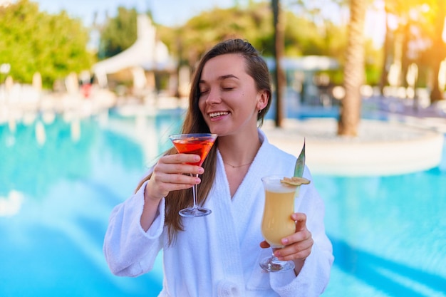 Jonge gelukkig lachende vrolijke vrouw geniet van zomervakanties met verfrissende pina colada en aperol cocktails bij het zwembad in het all-inclusive resort