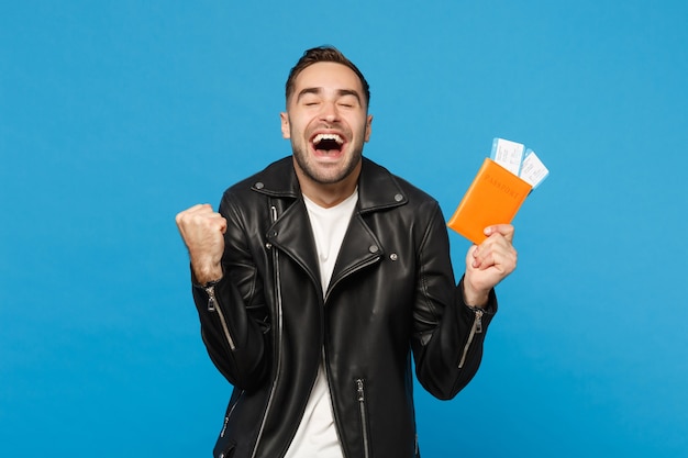 Jonge gelukkig ongeschoren man in zwarte jas wit t-shirt in de hand houden paspoort tickets geïsoleerd op blauwe muur achtergrond. passagier die naar het buitenland reist. lucht vlucht reis concept mock up kopie ruimte