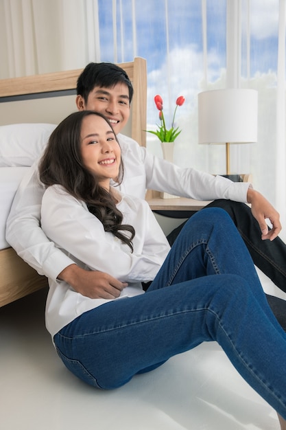 Jonge gelukkige aantrekkelijke Aziatische paar knuffelen samen zittend op de vloer in de slaapkamer.