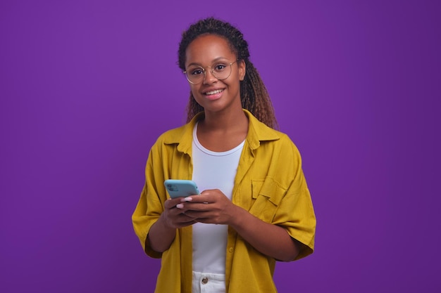 Jonge gelukkige Afrikaanse Amerikaanse vrouw met telefoon die en camera glimlacht bekijkt