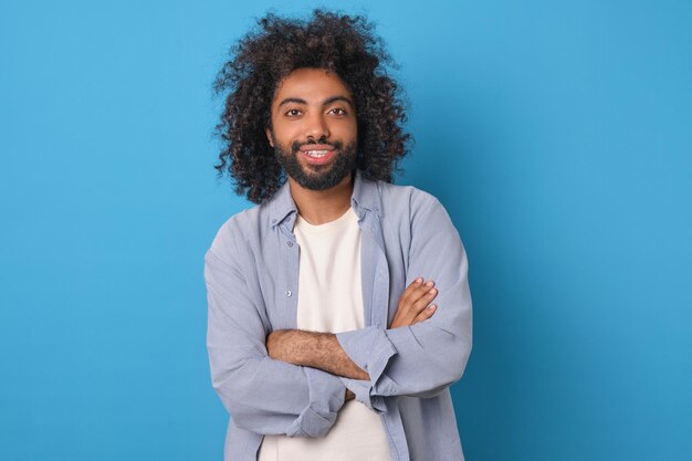 Jonge gelukkige Arabische man met de armen gekruist voor de borst staat in de studio