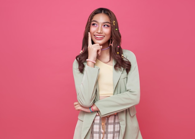Jonge gelukkige aziatische tienervrouw die iets denkt geïsoleerd op roze studioachtergrond
