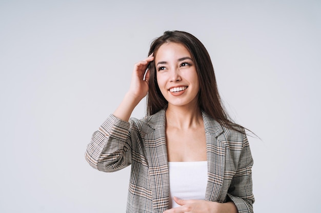 Jonge gelukkige aziatische vrouw met lang haar in pak op grijze achtergrond