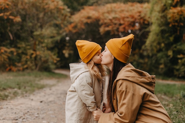 Jonge gelukkige en lachende moeder met haar dochtertje in de armen knuffelen en kussen een weekend doorbrengen met een wandeling in het herfstpark selectieve focus geluidseffect Herfststemming