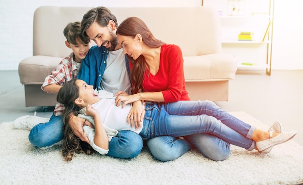 Jonge gelukkige familie die samen thuis ontspant, lacht en knuffelt elkaar terwijl ze op de vloer liggen